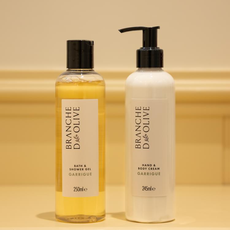 Branche d'Olive Garrigue bath/shower lotion shown next to Garrigue hand/boy lotion against a cream background.