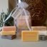Branche d'Olive guest soaps. Six are shown bagged in white voile with a hanging tag and six are shown outside the bag. The image is set against a backdrop of a jar containing dried olive leaves.