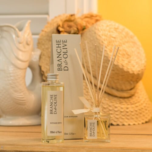 Branche d'Olive Bergamot Room Diffuser and Refill on a wooden table next to a fish glug glug water jug and straw hat