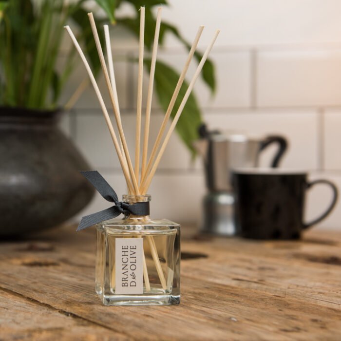 Branche d'Olive Room Diffuser in Olive Wood fragrance on a wooden table with coffee percolator and mug in the distance.