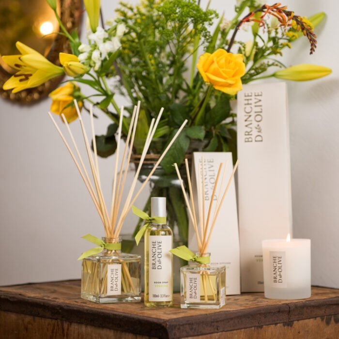 Branche d'Olive Verbena large and small Room Diffusers, Candle and Room Spray on a wooden table in front of some yellow flowers