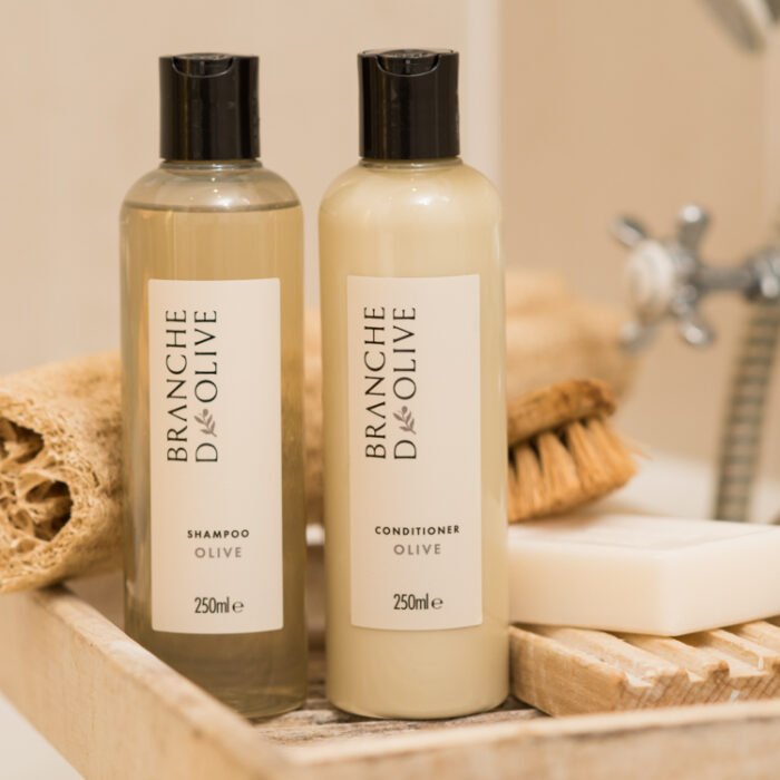 Bottles of Branche d'Olive Olive fragranced Shampoo and Conditioner a wooden bath caddy in a bathroom